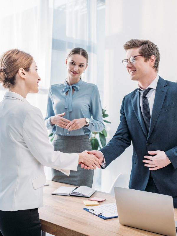 cheerful-recruiter-shaking-hands-with-woman-near-colleague-in-office.jpg